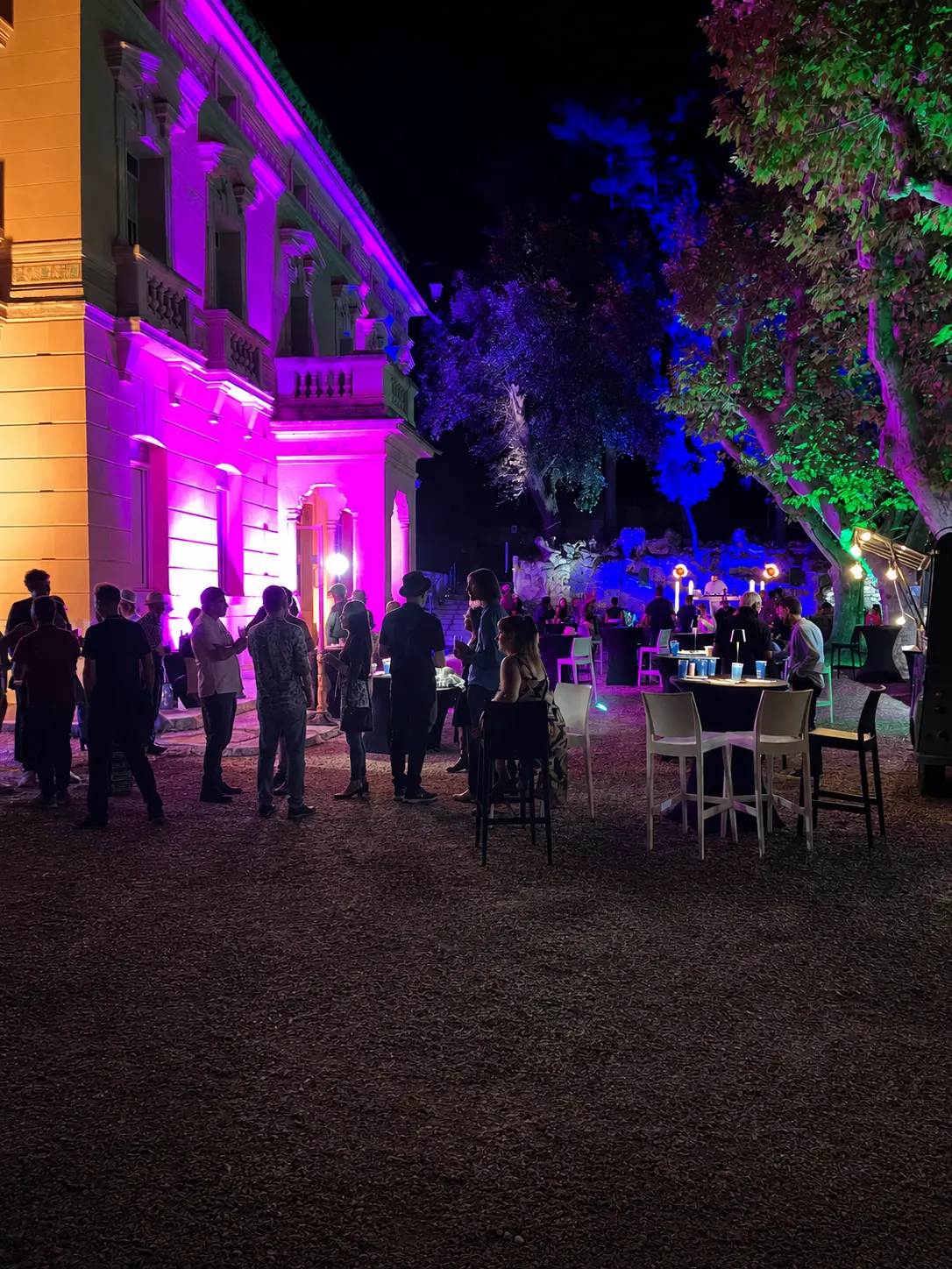 Façade de bâtiment et arbres mis en lumière colorée (rose, bleu, vert) lors d'un événement en soirée