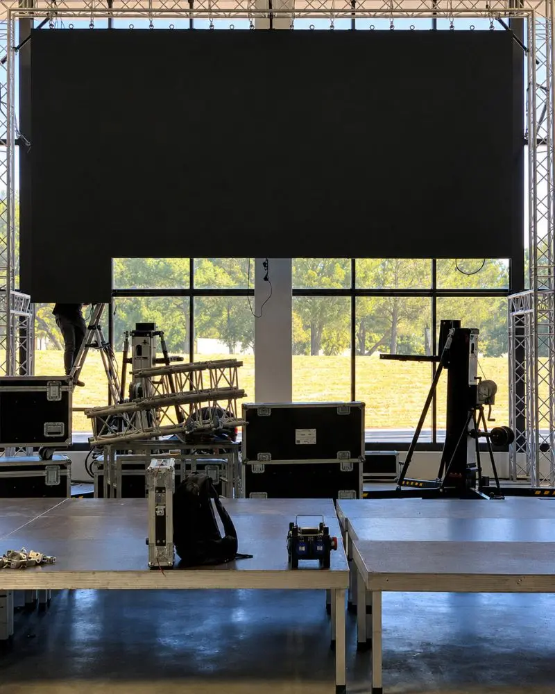 Montage d'un pont de structure avec écran suspendu, plateforme scénique et flight cases au sol